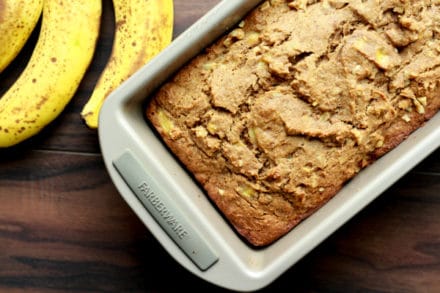 banana bread in a loaf pan with ripe bananas on the side