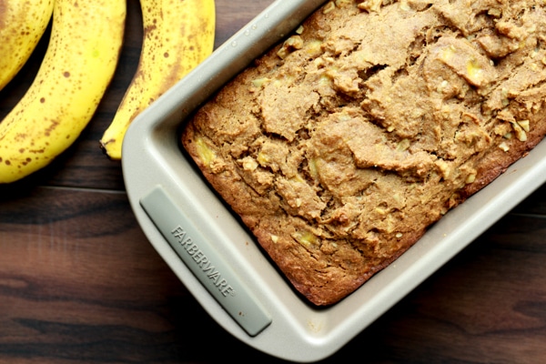 banana bread in a loaf pan with ripe bananas on the side
