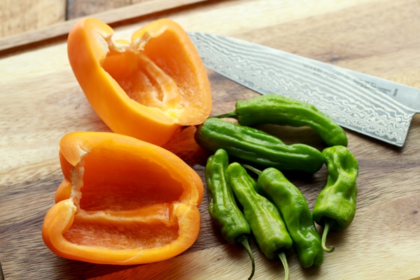 yellow bell peppers and shishito peppers on a wooden board with a chefs knife