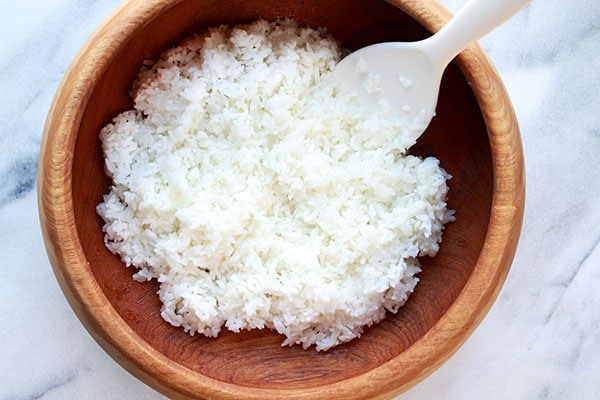 sushi rice in a wooden bowl and white paddle on a marble surface