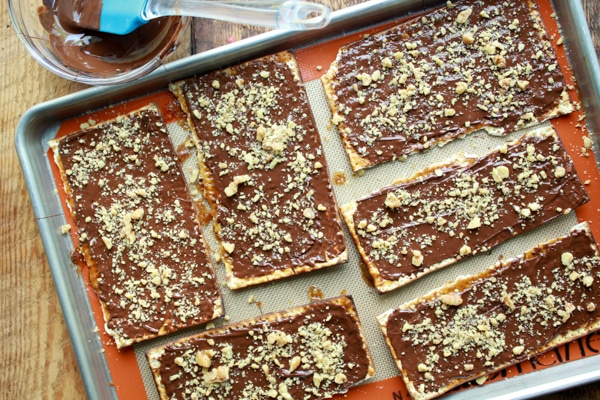 Pieces of chocolate covered Passover matzo on a baking sheet with a bowl of melted chocolate on the side