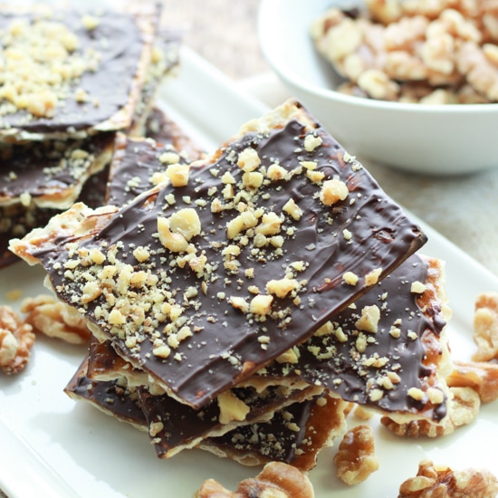 chocolate covered matzo on a white plate with sprinkles of walnuts on top