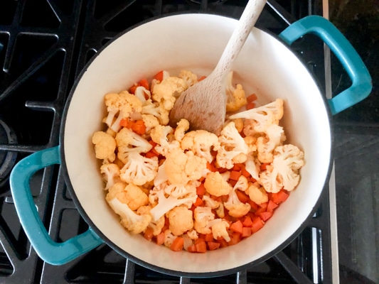 cauliflower florets and chopped carrots in a blue soup pot on the stove