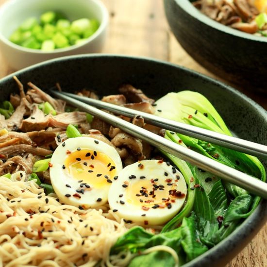 a bowl of pulled pork ramen topped with a runny egg and silver chopsticks