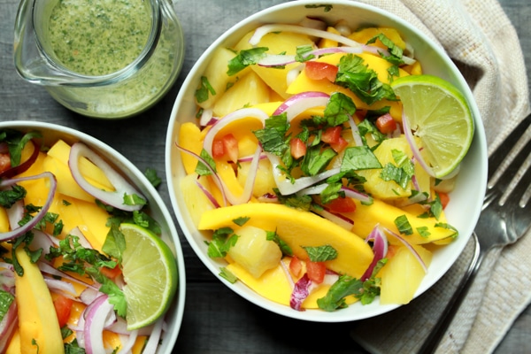 vibrant mango and pineapple salad in white bowls with lime vinaigrette on the side