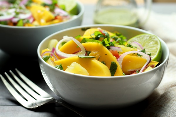 vibrant mango and pineapple salad in white bowls with lime vinaigrette on the side