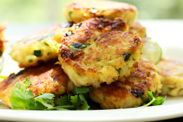 a stack of mini crab cakes on a white plate garnished with fresh cilantro sprigs