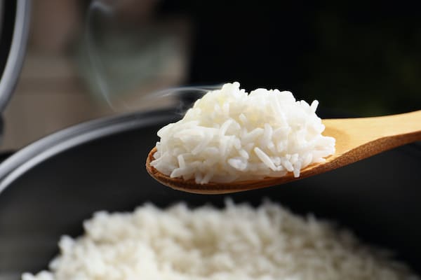 Steamed white rice on a wooden spoon held above a rice cooker