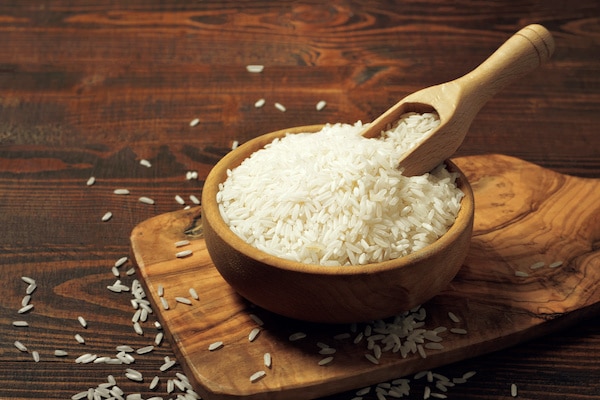 uncooked white rice kernels in a wooden bowl on top of a wooden cutting board