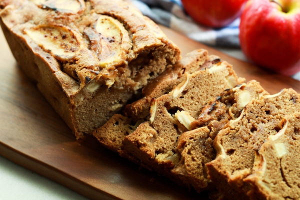 slices of apple ginger bread on a wooden board with red apples in the background
