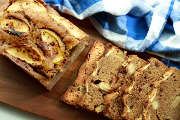 slices of apple ginger bread on a wooden board next to a blue and white checkered napkin