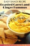a small bowl of roasted carrot and ginger hummus with a pita chip inserted and pita chips on the side