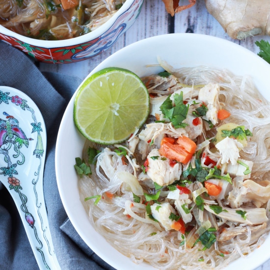 A white bowl with turkey noodle soup with a slice of lime and a spoon on the side