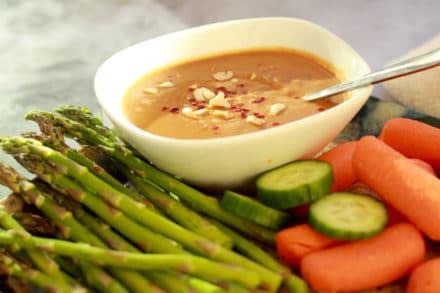peanut sauce inside a small white bowl surrounded by fresh vegetables