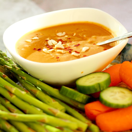 peanut sauce inside a small white bowl surrounded by fresh vegetables