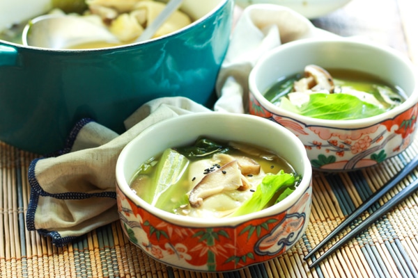 two bowls filled with vibrant wonton soup with chopsticks on a bamboo placemat