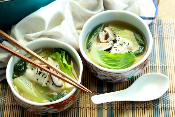 two bowls filled with wonton soup and chopsticks and a white spoon on the side