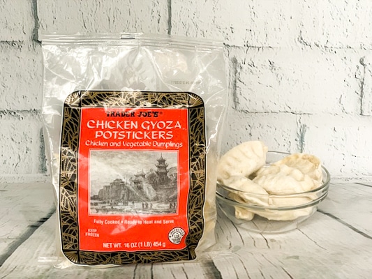 a bag of Trader Joe's frozen Chicken Gyoza Potstickers on a white board with a glass bowl filled with potstickers on the side