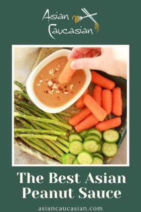 A woman's hand dipping a carrot into a small white bowl of peanut sauce on a tray with fresh vegetables