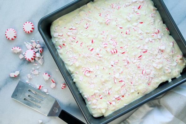 A square cake pan filled with peppermint brownies with white chocolate frosting and sprinkles of peppermint candy on top