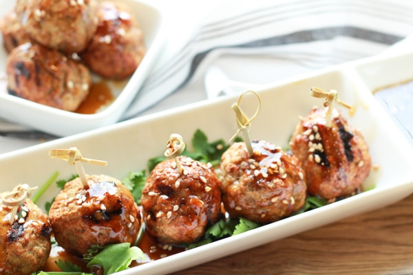 shrimp and turkey meatballs on top of greens on a narrow white plate with a side of Asian dipping sauce