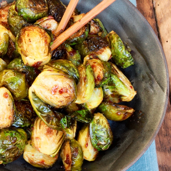 Roasted Brussels sprouts in a blue bowl with chopsticks on top of a wooden board