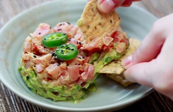 A woman scooping up Ahi tuna napoleon dip on a gray plate with sesame chips.