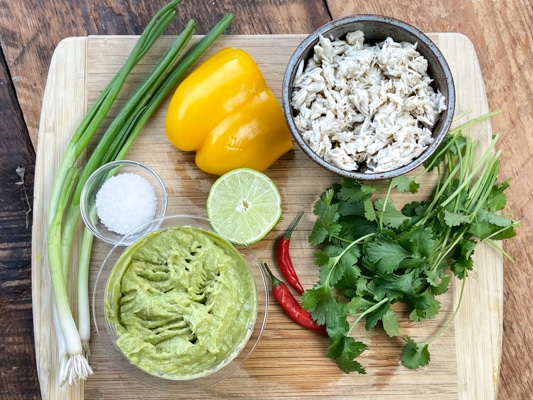 Ingredients for spicy crab wonton cups with guacamole on a wooden cutting board.