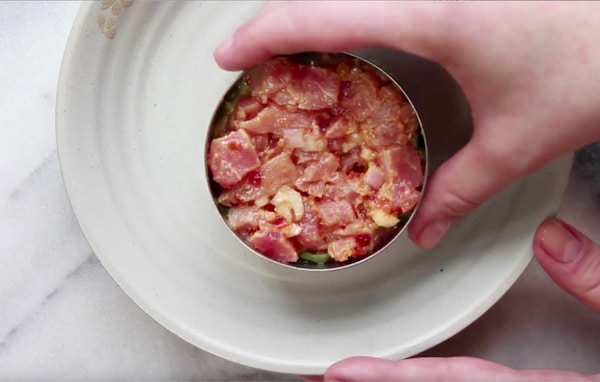 A woman removing the ring mold from Ahi tuna napoleon on a white plate.