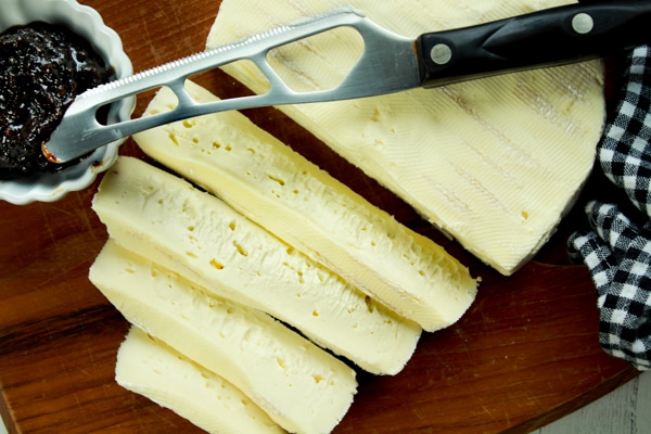 Slices of brie on a cutting board with a side of fig jam and a cheese knife.