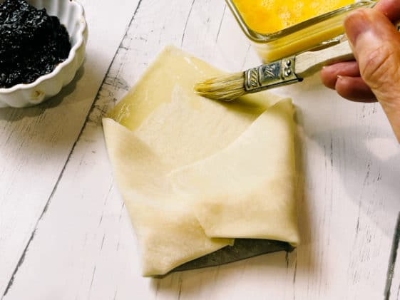 A woman brushing an egg wash on a folded wonton wrapper on top of a white board.