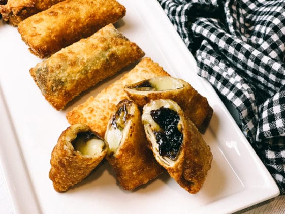 Crispy, golden spring rolls filled with brie and fig on a long white serving platter.