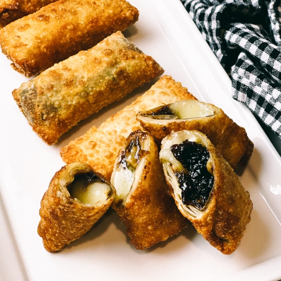 Crispy, golden spring rolls filled with brie and fig on a long white serving platter.