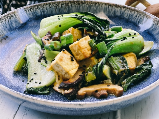 Stir-fry miso shiitake mushrooms, tofu, and baby bok choy on a blue plate.