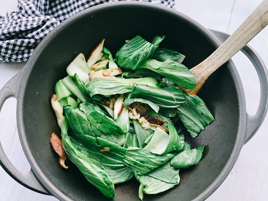 Stir fry vegetables in a black wok: baby bok choy, shiitake mushrooms and shallots.