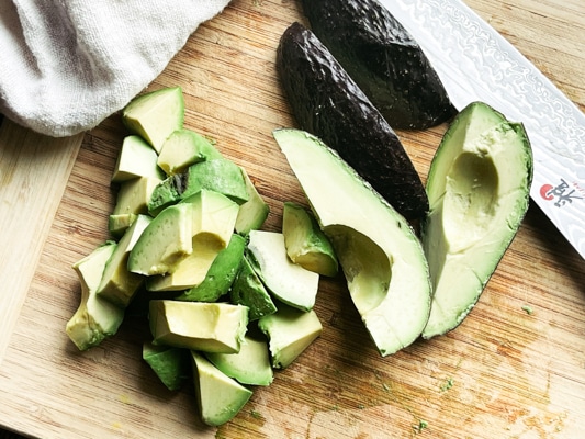 Chopped avocado on a wooden cutting board with a chef's knife and napkin along side.