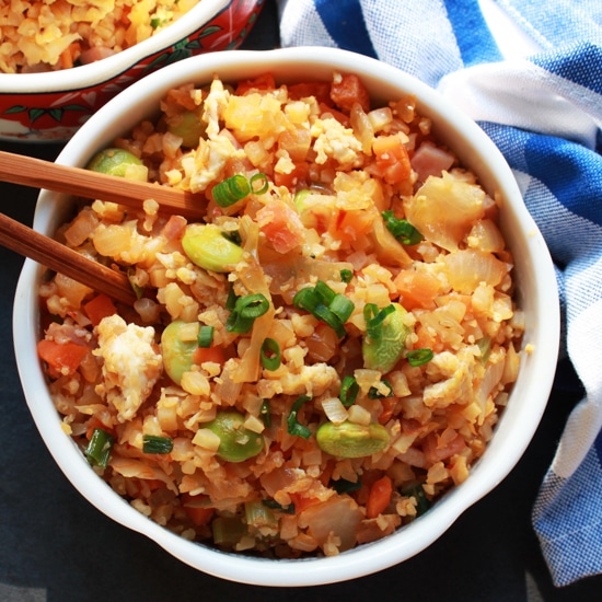 A bowl of Kimchi cauliflower fried rice with chopsticks and blue and white napkin on the side