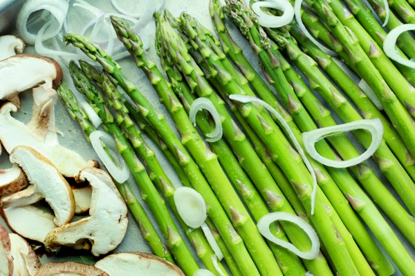Fresh asparagus and shiitake mushrooms on a tray with shallot rings on top
