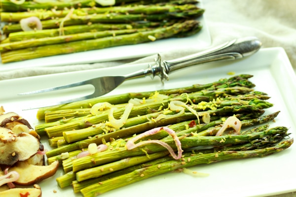 Roasted asparagus and shiitake mushrooms on two white trays with a serving fork on the side.