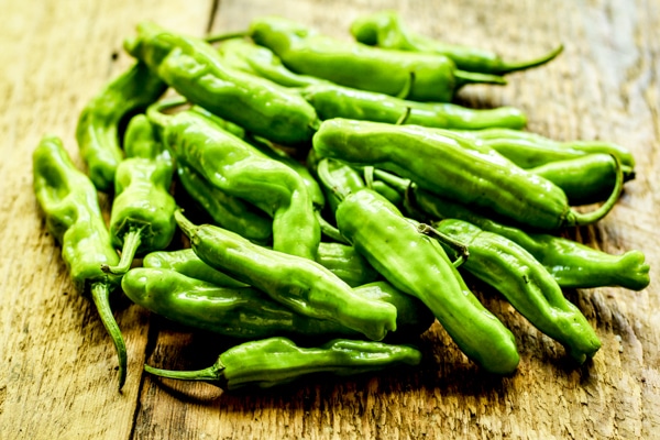 Fresh green shishito peppers in a pile on a wooden board.