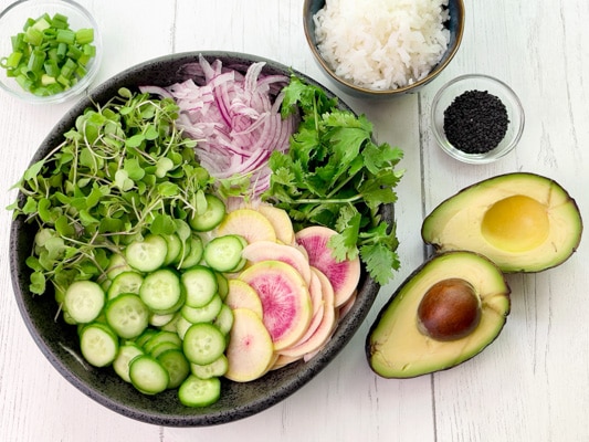 Veggie ingredients for a miso tofu poke bowl nestled inside a large black bowl with avocado halves and white rice on the side.