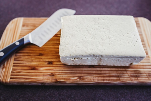 A block of extra firm tofu on wooden cutting board with a chef's knife