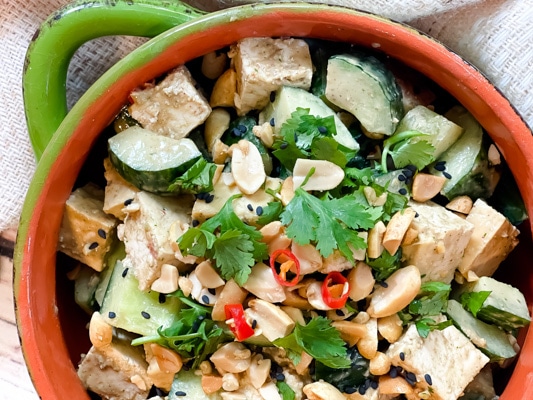 A green bowl filled with a vibrant spicy Asian tofu salad with cucumbers, cilantro, and peanuts.