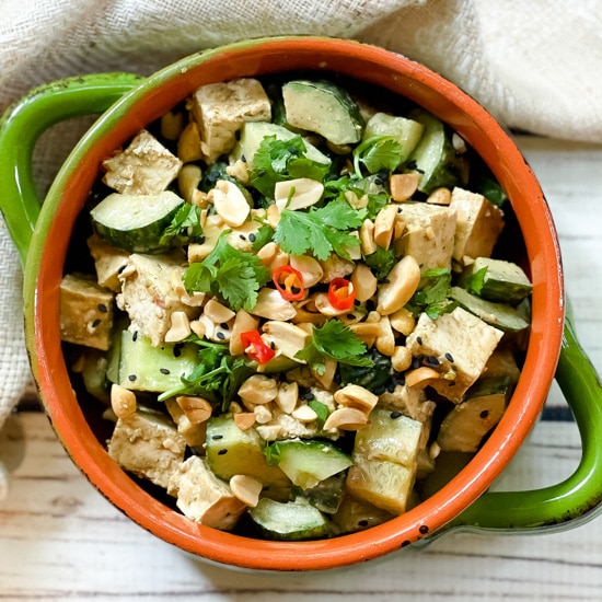 A green bowl filled with a vibrant spicy tofu salad with cucumbers, cilantro and peanuts.