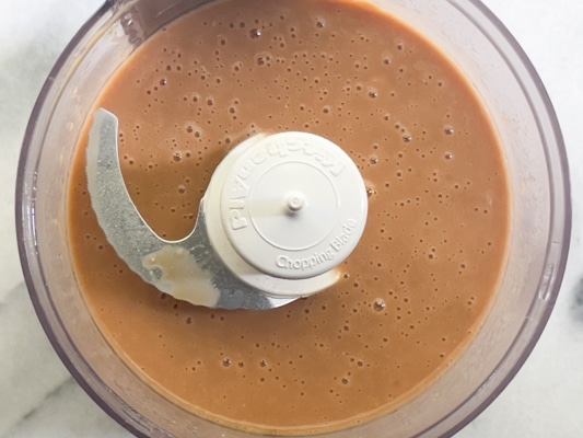 A small food processor with the lid filled with miso dressing that's been puréed.