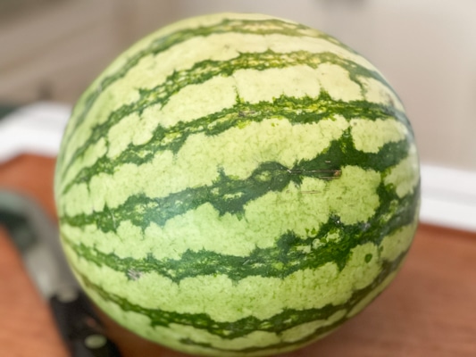 A whole round watermelon on top of a wooden board.