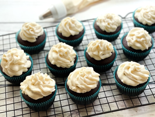 Frosted chocolate miso cupcakes on top of a black wire rack with a piping bag in the background.