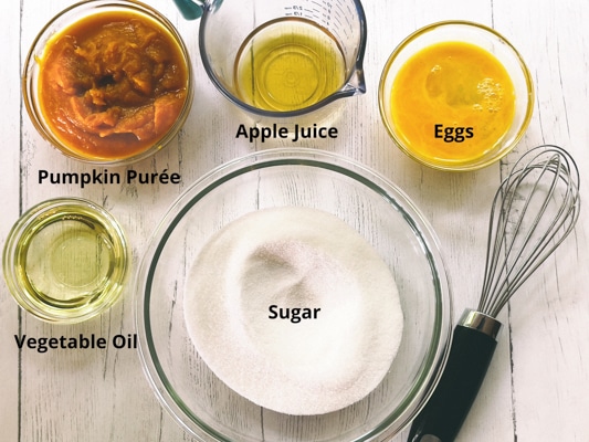 Ingredients for making pumpkin muffins on top of a white board with a whisk on the side.