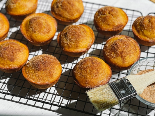 Freshly baked pumpkin muffins on a wire baking rack with a basting brush on the side.