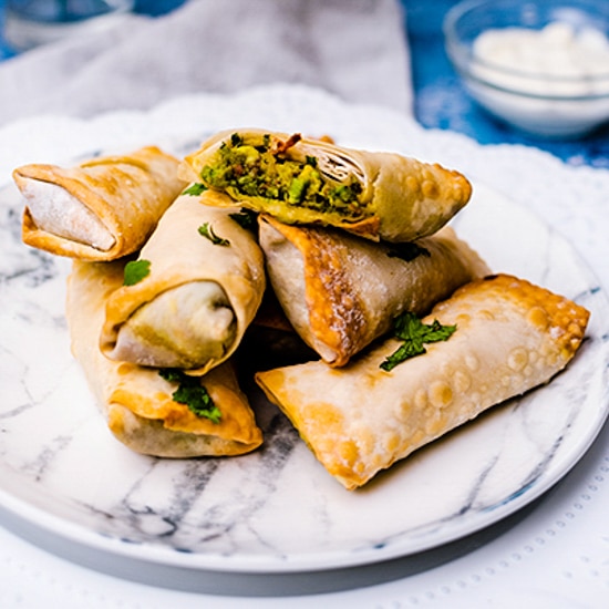 Vegan Avocado Egg Rolls stacked on a white marbled plate on top of a blue board with a small bowl of sour cream in the background.